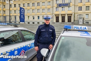 policjant stoi obok dwóch radiowozów.