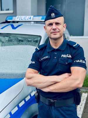 Umundurowany policjant stoi przy radiowozie.