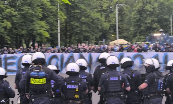 po jednej stronie stoją policjanci, po drugiej kibice.