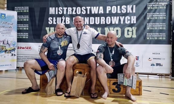 Zdjęcie przedstawia zawodników siedzących na podium.