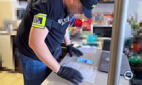 Policjant CBZC pochyla się nad leżącymi na stole dokumentami i telefonem.
