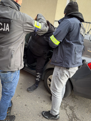 Dwaj nieumundurowani policjanci z zatrzymanym, który wysiada z auta.