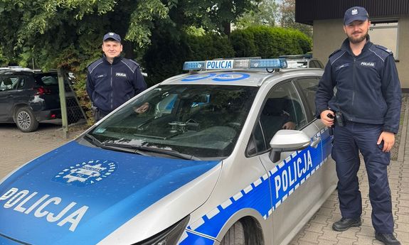Dzielnicowi przy radiowozie, w tle widać drzewa.