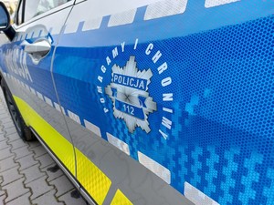 Hasło pomagamy i chronimy oraz grafika policyjnej gwiazdy na niebieskim pasie bocznym radiowozu.