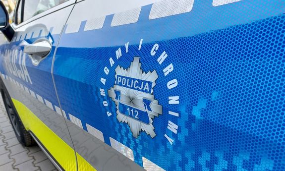 Hasło pomagamy i chronimy oraz grafika policyjnej gwiazdy na niebieskim pasie bocznym radiowozu.