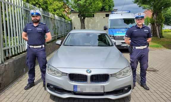 Dwaj umundurowani policjanci przy bmw. Z tyłu widać policyjny radiowóz.