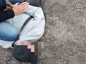 Mężczyzna leżący na ziemi skuty kajdankami.