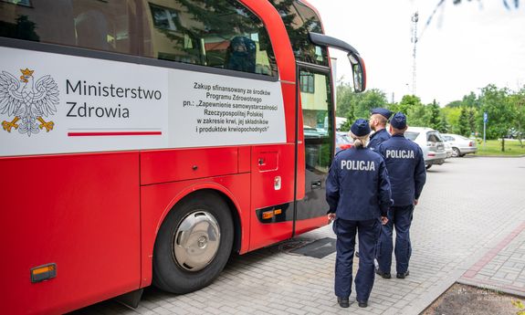 Umundurowani policjanci stoją przed krwiobusem.