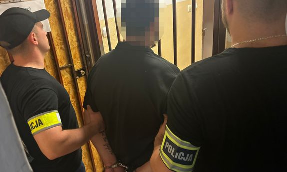 Zatrzymany mężczyzna prowadzony przez dwóch nieumundurowanych policjantów.
