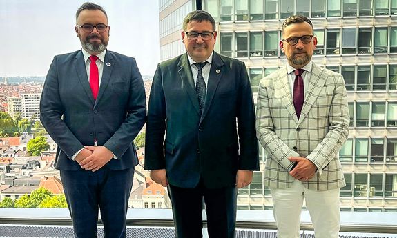 Trzej mężczyźni w  garniturach pozują do zdjęcia.