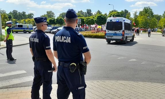 Policjanci na ulicy zabezpieczają wydarzenie, na drugim planie widoczne są policyjne radiowozy.