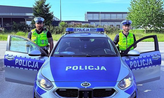dwóch policjantów stoi koło radiowozu.