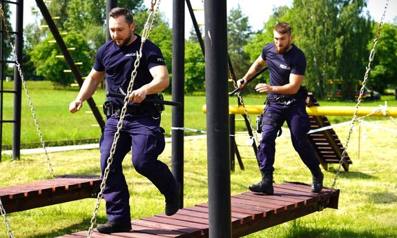 dwóch policjantów biegnie po kładce na torze przeszkód.