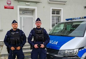 dwóch policjantów stoi obok radiowozu i pozują do zdjęcia.