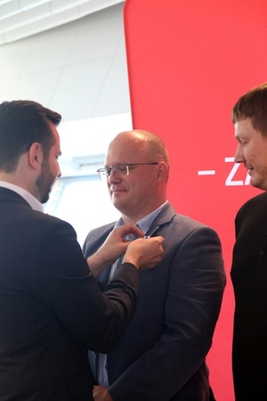 Mężczyzna w garniturze przypina odznaczenie drugiemu mężczyźnie.