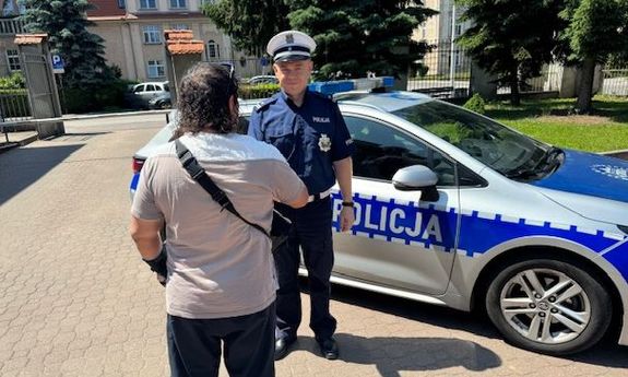 Mężczyzna dziękuje policjantom stojącym przy radiowozie.