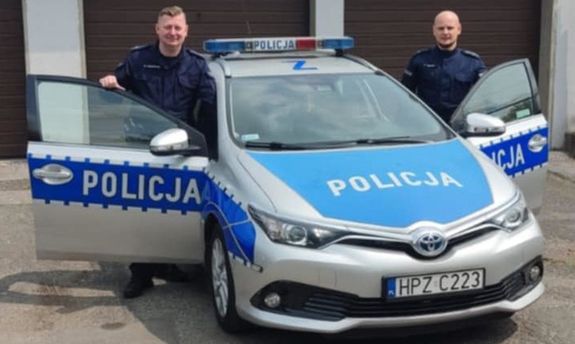 Dwaj umundurowani policjanci w drzwiach radiowozu.