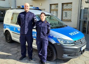 Dwoje umundurowanych policjantów przed radiowozem.
