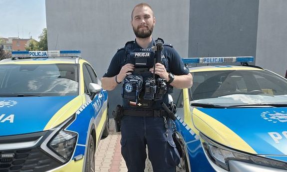 policjant stoi między dwoma radiowozami.