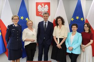 Na zdjęciu pięć kobiet, z których jedna jest w mundurze policyjnym oraz jeden mężczyzna. W tle flagi Unii Europejskiej i Polski oraz godło Polski.