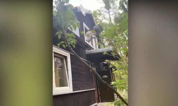 Młody człowiek wyrzuca przez okno domu telewizor.