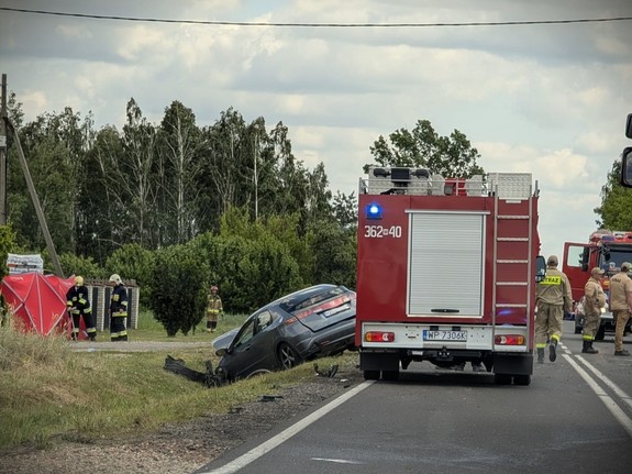 Samochód w rowie. Na jezdni widać wóz strażacki i funkcjonariuszy.