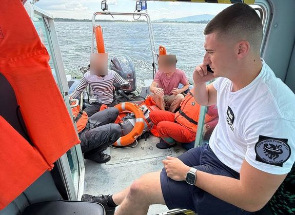 Na zdjęciu policjant we wnętrzu łodzi. Za nim w tle cztery osoby