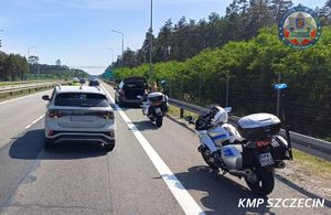 Stojące na poboczu drogi auto, za nim dwa policyjne motocykle, a obok na jezdni widać przejeżdżające pojazdy.