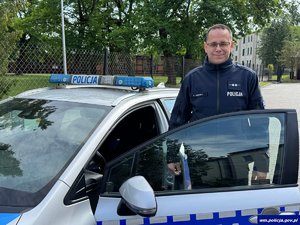 policjant stoi przy radiowozie.