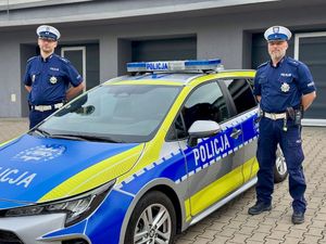 Dwaj umundurowani policjanci, którzy pomogli dojechać Wojtusiowi do szpitala, stoją przy radiowozie.
