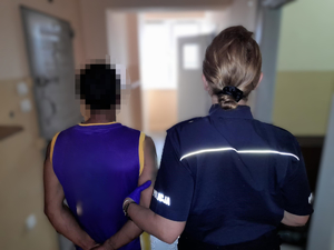 Policjantka z zatrzymanym mężczyzna zakutym w kajdanki.