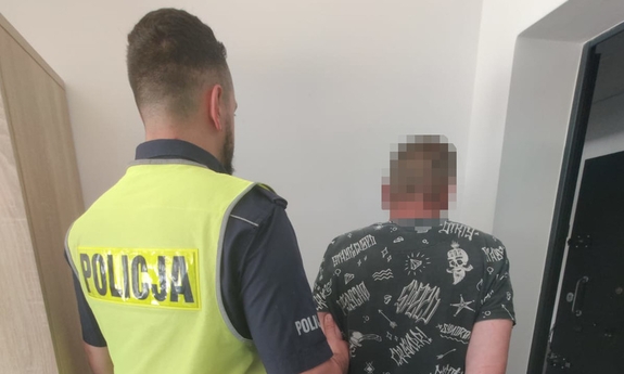 Zatrzymany mężczyzna w kajdankach prowadzony przez policjanta.