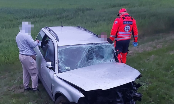 Rozbity pojazd na skraju pola. Przy pojeździe nieumundurowany policjant i ratownik medyczny.