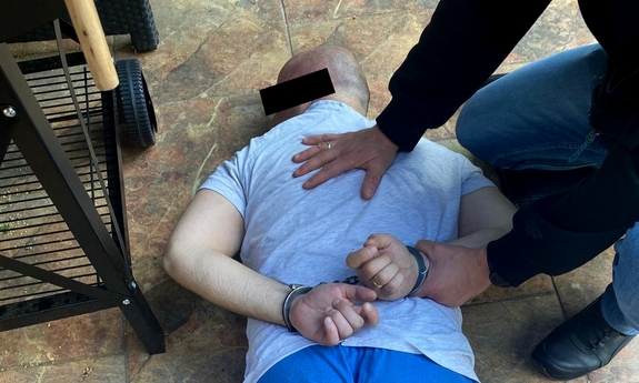 Zatrzymany leży na podłodze zakuty w kajdanki, trzyma go policjant.