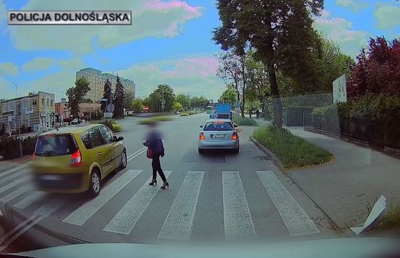 Stop klatka z monitoringu: pieszy przechodzi przez przejście na pasach i przejeżdża auto.