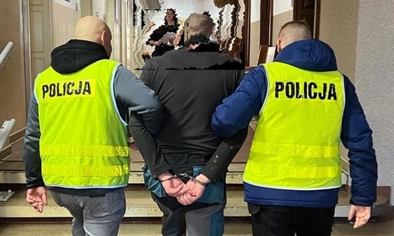 Dwaj funkcjonariusze prowadza zatrzymanego mężczyznę.
