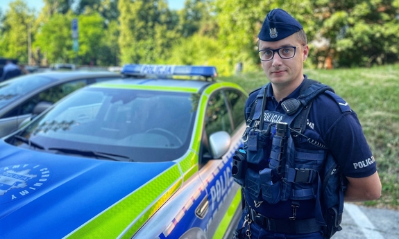 Policjant stoi przy radiowozie.