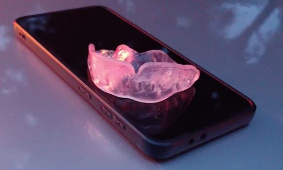 Na stole leży telefon. Na nim leży ochraniacz na zęby.