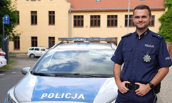 Umundurowany policjant przy radiowozie.