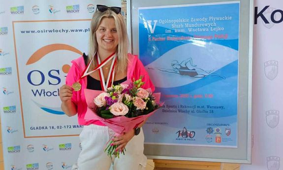 Ubrana w dres policjantka z medalami na szyi i z bukietem kwiatów.