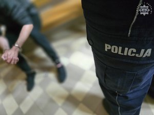 Zatrzymany mężczyzna w kajdankach siedzi na ławce.