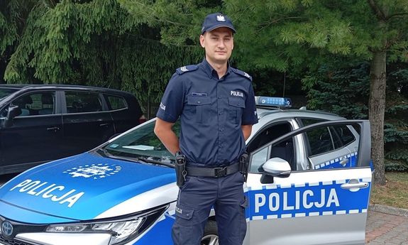 Umundurowany policjant przy radiowozie.