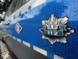 Z boku na drzwiach policyjnego radiowozu widać logo ruchu drogowego i policyjną odznakę z numerem 112.