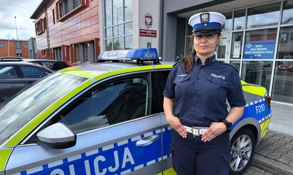 Policjantka ruchu drogowego stoi przy radiowozie w tle budynek.