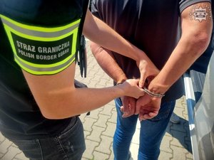 Funkcjonariusz Straży Granicznej zakłada kajdanki zatrzymanemu.