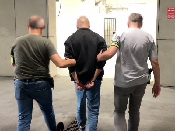 Dwaj nieumundurowani policjanci prowadzą zatrzymanego.