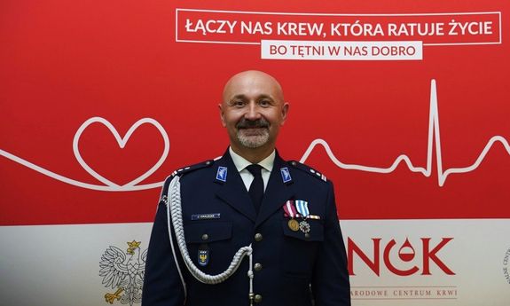POLICJANT POZUJE NA TLE TABLICY &quot;ODDAWANIA KRWI&quot;.