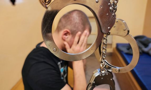 Kajdanki zespolone i mężczyzna zasłaniający dłońmi twarz.