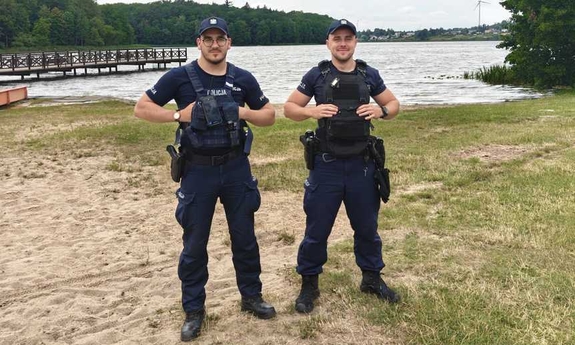 Dwaj policjanci stoją na brzegu zbiornika wodnego.