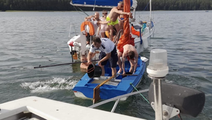 Żaglówka na jeziorze - policjant wylewa z niej wodę.